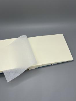 Preview: Fotoalbum 15×21 cm quer Möwenflug – aufgeschlagene Seite mit leinenstrukturiertem Pergaminblatt über weißem Fotokarton