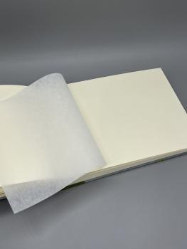 Preview: Fotoalbum 15×21 cm quer Kleiner Prinz – aufgeschlagene Seite mit leinenstrukturiertem Pergaminblatt über weißem Fotokarton
