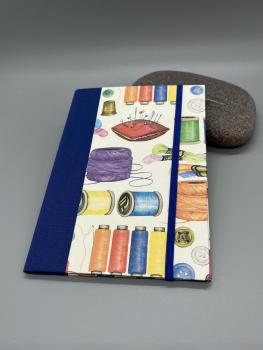 Handgebundene Klemm-Mappe A6 Nähutensilien – Frontdeckel mit Garnrollen-Motiv, blauer Leinenrücken und Gummikordel